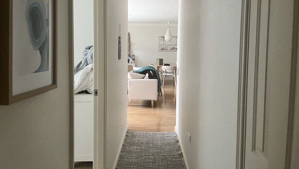 Un couloir étroit mène à une chambre qui contient un lit, une chaise et une table.