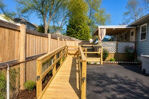 A wooden deck leading to a covered outdoor area with a white lattice fence and a small garden. - Modern Halethorpe Home. Sleeps 8. 4 Beds. Near BWI, UMBC & Baltimore (halethrope)