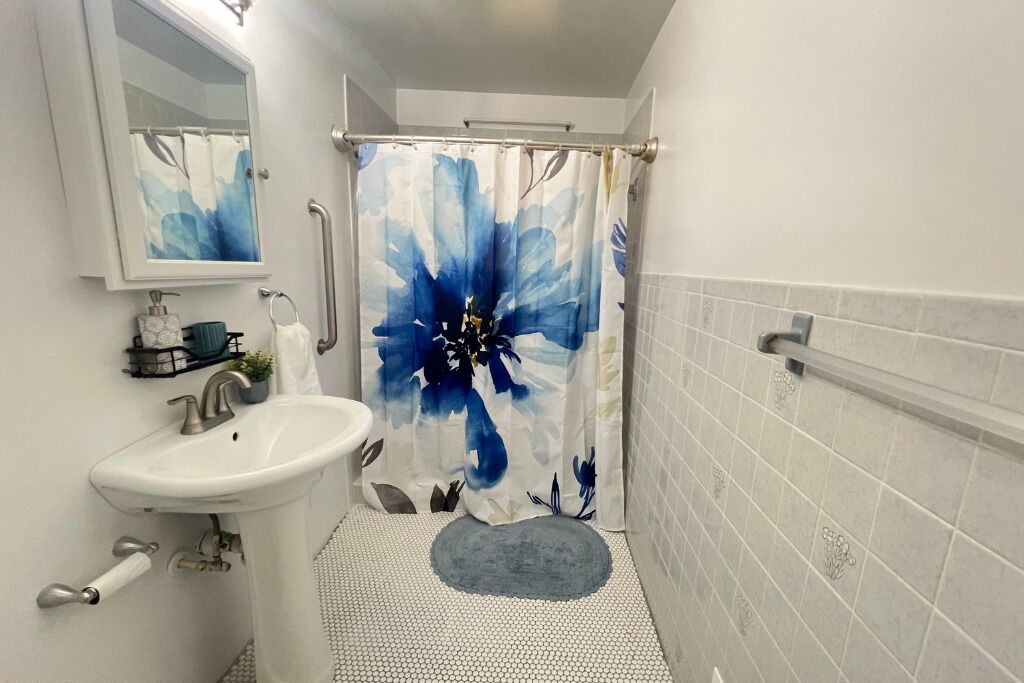 A bathroom with a white sink, a mirror, a shower with a blue floral curtain, and a tiled floor.