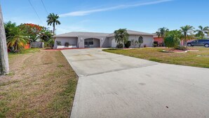 Une maison d’habitation avec une allée, un garage et une pelouse agrémentée de palmiers.