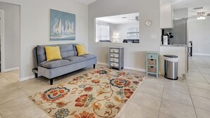Un salon avec un canapé gris, un tapis coloré et un tableau représentant des voiliers.
