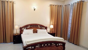 A neatly made bed with a wooden headboard, two bedside lamps, and curtains on either side. - Sant Niwas Shahpur 3BHK Villa (Mohali)