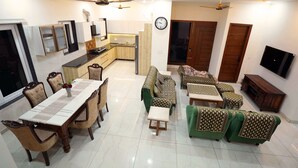 A modern living room with a dining area, green sofas, a kitchen, and a TV mounted on the wall. - Sant Niwas Shahpur 3BHK Villa (Mohali)
