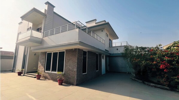 A modern two-story house with a balcony, a garage, and potted plants.