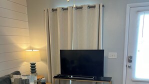 Una sala de estar con un sofá gris, un televisor sobre un mueble, una lámpara y cestas de almacenamiento.