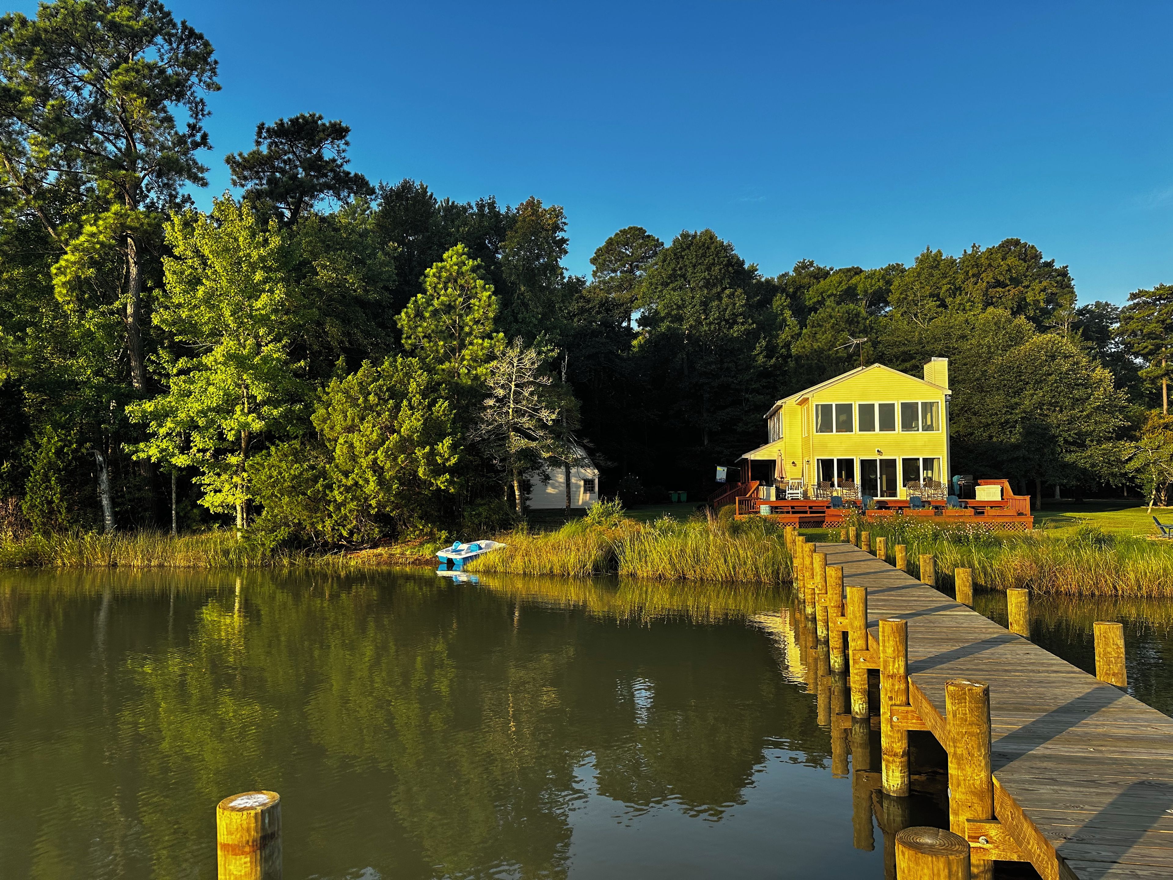 Une maison jaune avec un quai s’avançant dans un lac paisible, entourée d’arbres denses.