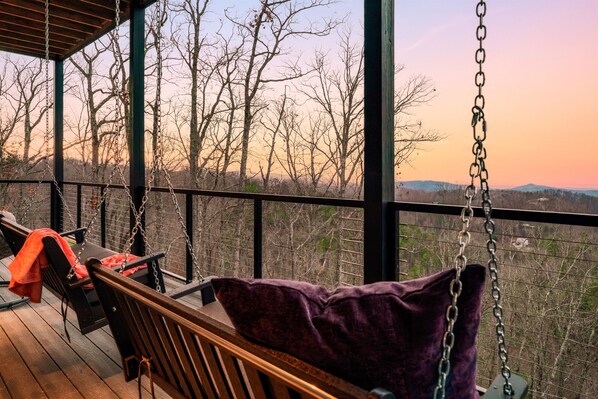 Une terrasse en bois avec une chaise suspendue et un banc, offrant une vue sur un paysage boisé.