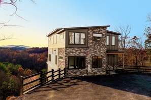 Una casa moderna de dos pisos amb façana de pedra, grans finestres i una terrassa de fusta.
