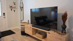 A modern living room with a large flat-screen TV on a wooden stand, a black sofa, a small coffee table, a black rug, and a decorative vase with dried plants. - Stay at Silver Mountain Drive (Nanaimo)