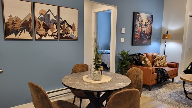 A dining area with a round table, four chairs, and a vase with plants. There is a sofa and a painting in the background. - Stay at Silver Mountain Drive (Nanaimo)