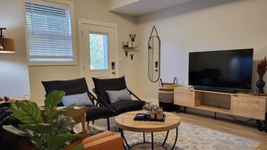 A modern living room with two black armchairs, a round coffee table, a TV on a wooden stand, and a large window with blinds. - Stay at Silver Mountain Drive (Nanaimo)