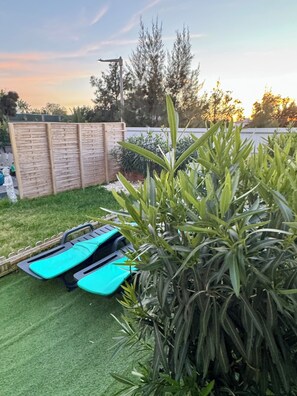 Un patio trasero con una valla de madera, césped verde y dos sillones azules.