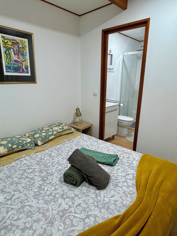 Une chambre à coucher avec un lit, une table de chevet, un miroir et une salle de bain visible à travers une porte ouverte.