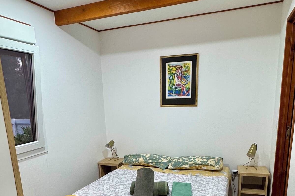 A bedroom with a bed, a window, a painting, and a wooden ceiling.