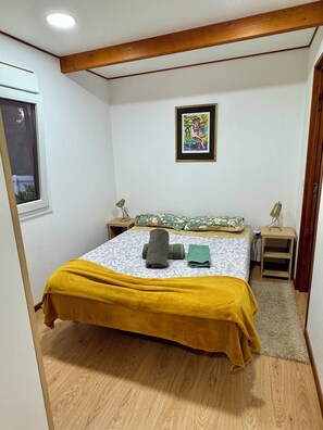 Un dormitorio con cama, ventana, cuadro y techo de madera.