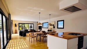 A modern kitchen with a central island, wooden flooring, and a dining area with chairs and a table.