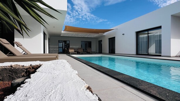 A modern pool area with a clear blue sky, white walls, and a minimalist design.