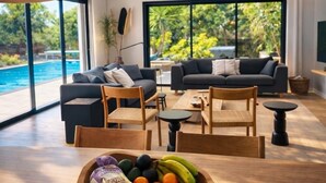 A modern living room with a pool view, wooden furniture, and a fruit bowl on the table.