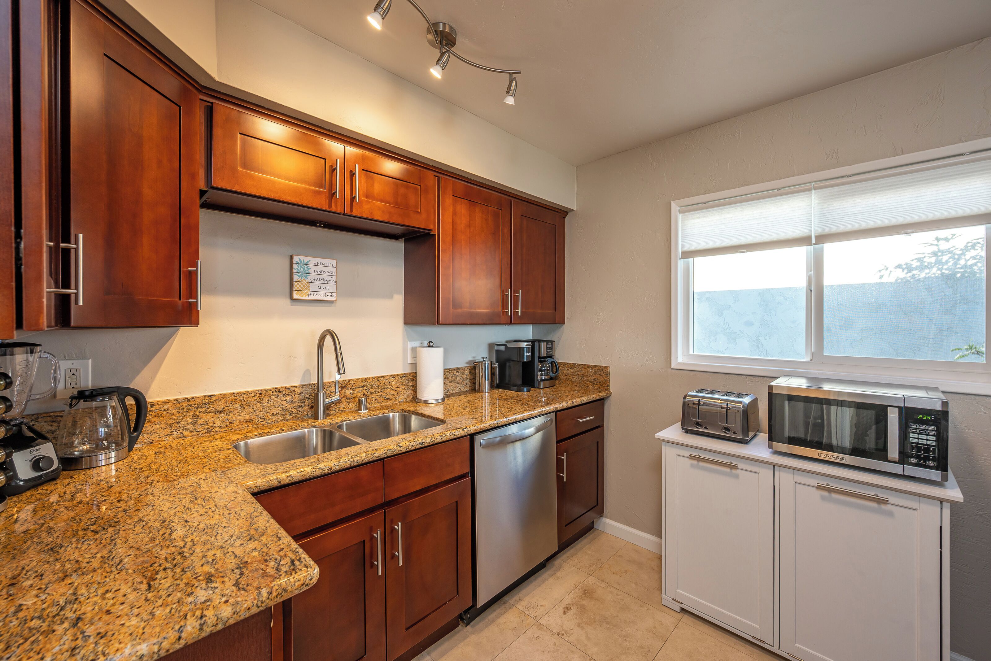 A kitchen with granite countertops, stainless steel appliances, wooden cabinets, and a window with blinds.