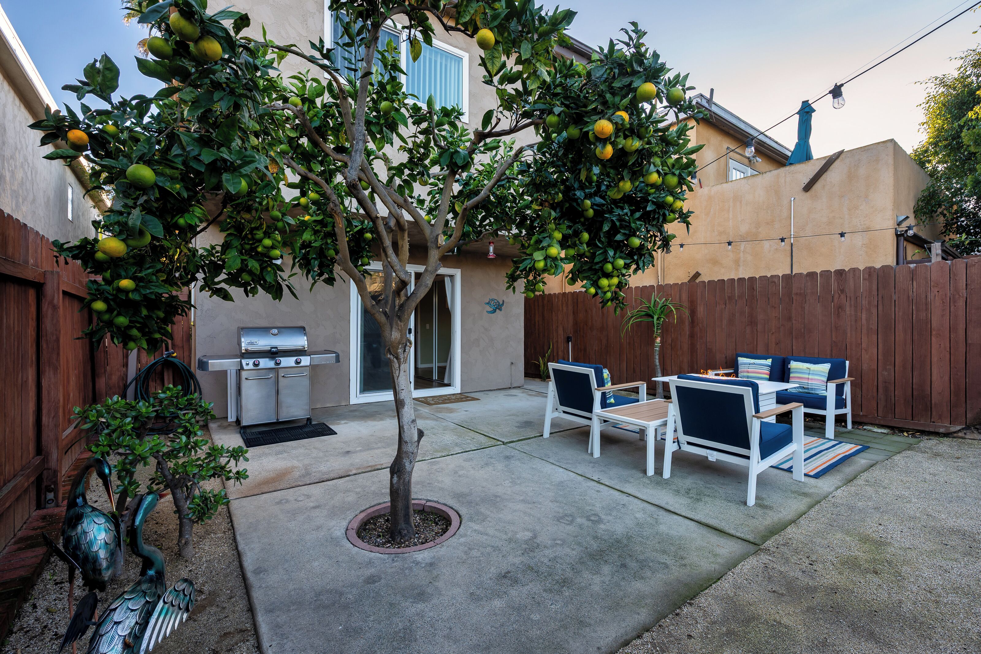 A backyard with a tree, patio furniture, and a grill.