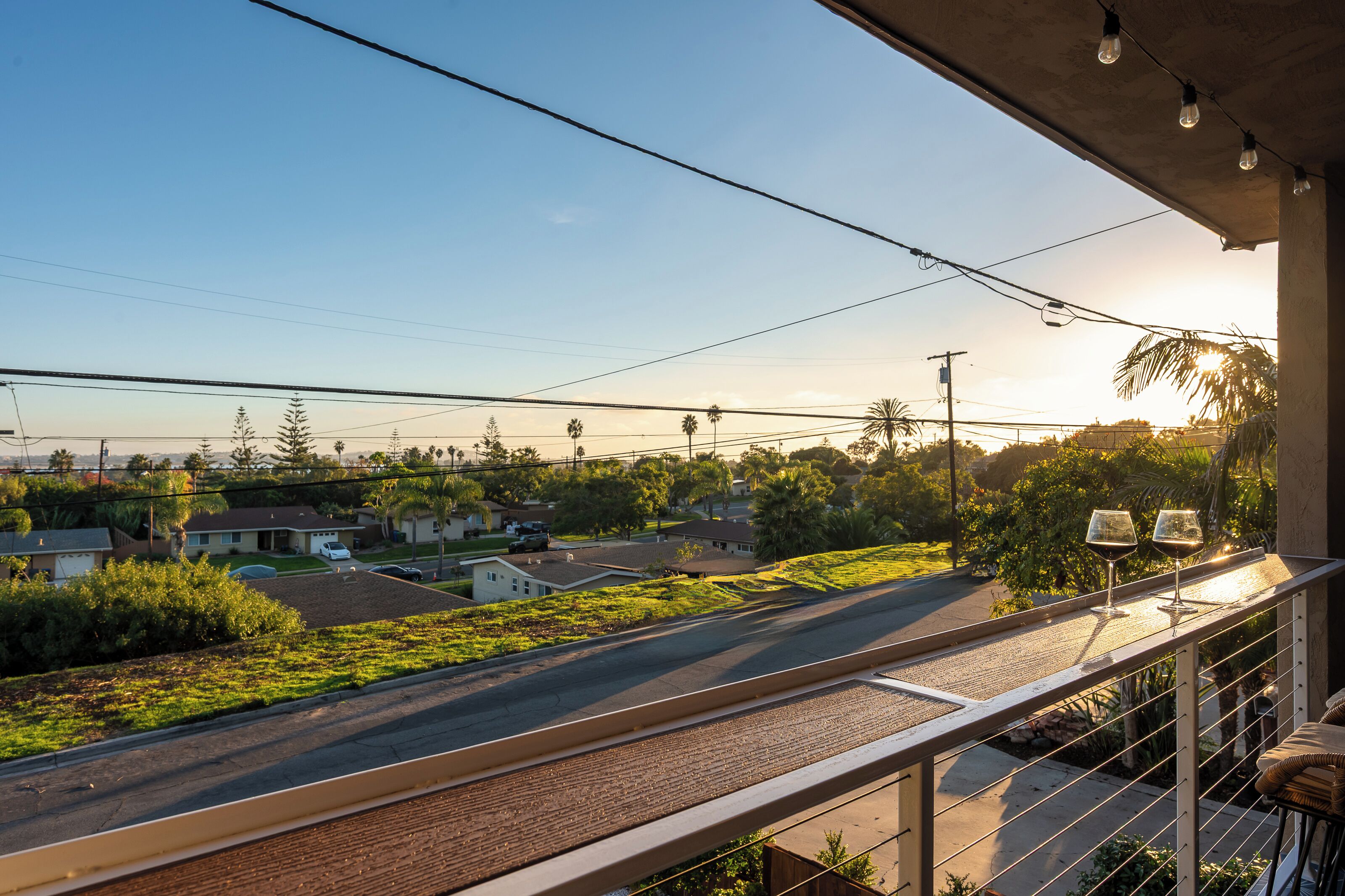 A balcony with a view of a residential street, power lines, and a clear sky.