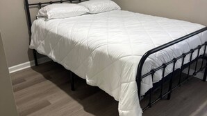 A single bed with a white duvet in a room with wooden flooring and plain walls. - Cozy 1-bedroom home in the heart of Jonesboro! (Jonesboro)