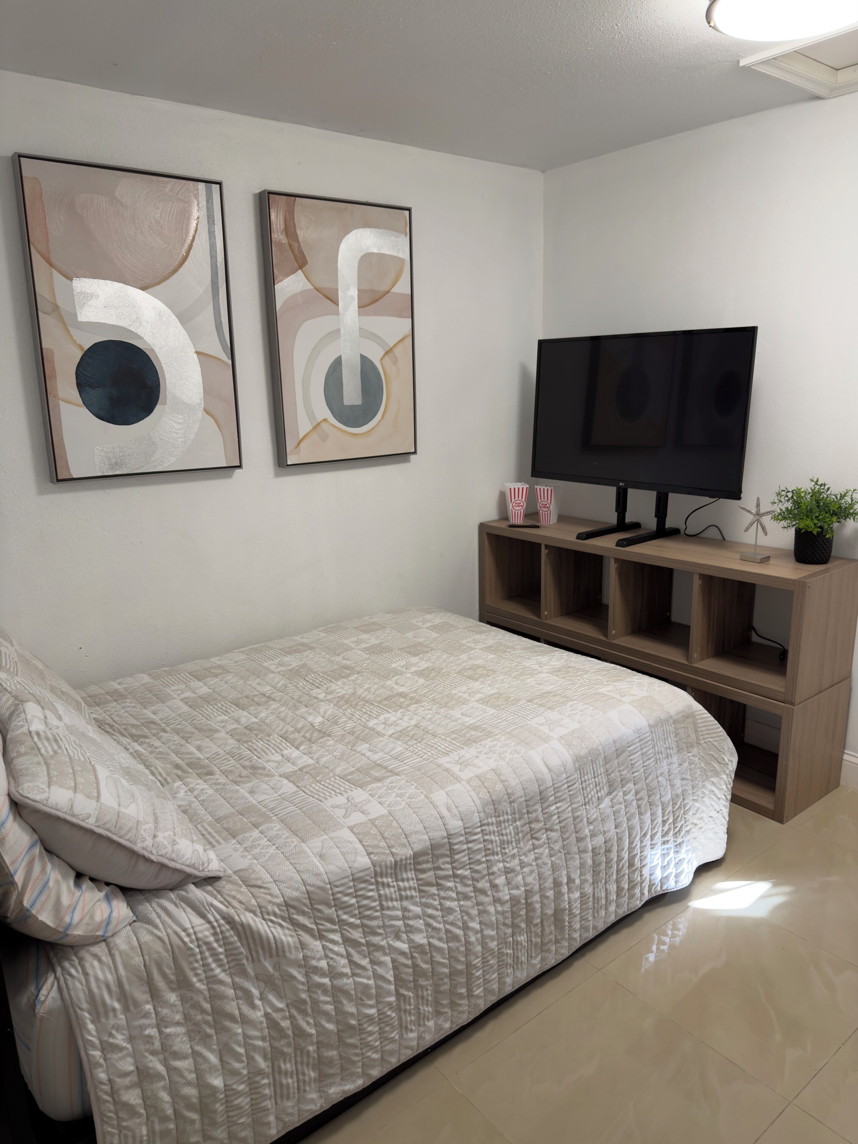 Un dormitorio con cama, televisión y dos cuadros abstractos en la pared.