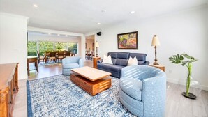 Ein modernes Wohnzimmer mit Sofa, Sessel, Couchtisch und Essbereich im Hintergrund.