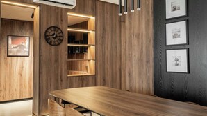 A modern dining area with a wooden table and chairs, a built-in shelf unit, and a wall-mounted clock. - Coral Luxe Suite - Spacious  Luxury 3 Bed Waterfront View in quiet VI cul-de-sac (Lagos)