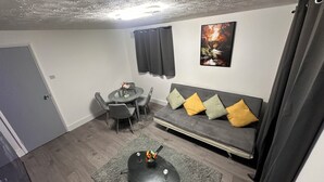 Ett modernt vardagsrum med en grå soffa, ett matbord med stolar och en tavla på väggen.