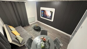 Ett modernt vardagsrum med en grå soffa, ett soffbord i glas och en tv som är monterad på en vägg med ett vertikalt panelmönster.