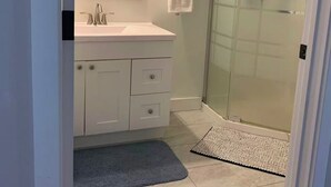 Een badkamer met een witte wastafel, een glazen douchecabine en een handdoek aan de muur.