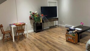 Een moderne woonkamer met een houten vloer, een eettafel met stoelen, een tv op een meubel en een bijzettafeltje met een bloevas.