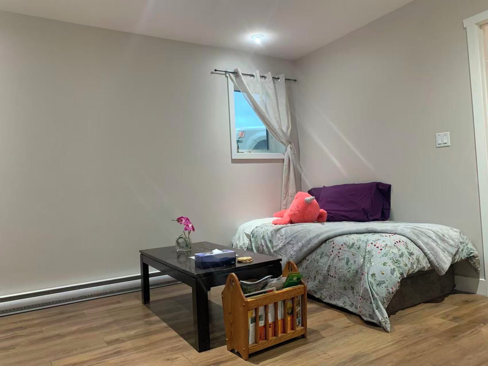 Un dormitorio con una cama, una mesita, una ventana con cortinas y suelo de madera.