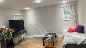 Een slaapkamer met een bed, een televisie, een tafeltje en een raam met gordijnen.