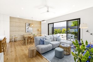 Un salon moderne avec un canapé d’angle gris, une table à manger en bois et une grande fenêtre donnant sur un jardin.