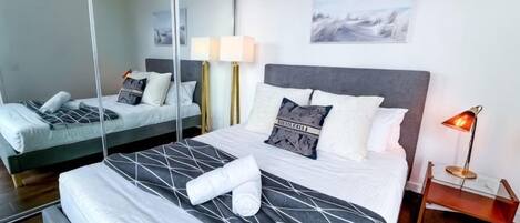 A hotel room with a large bed, a bedside table with a lamp, a mirror, and a painting on the wall.