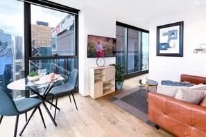 A modern living room with a glass table, chairs, a sofa, and a TV. - LV42 High-rise condo CBD panoramic city view (Melbourne)