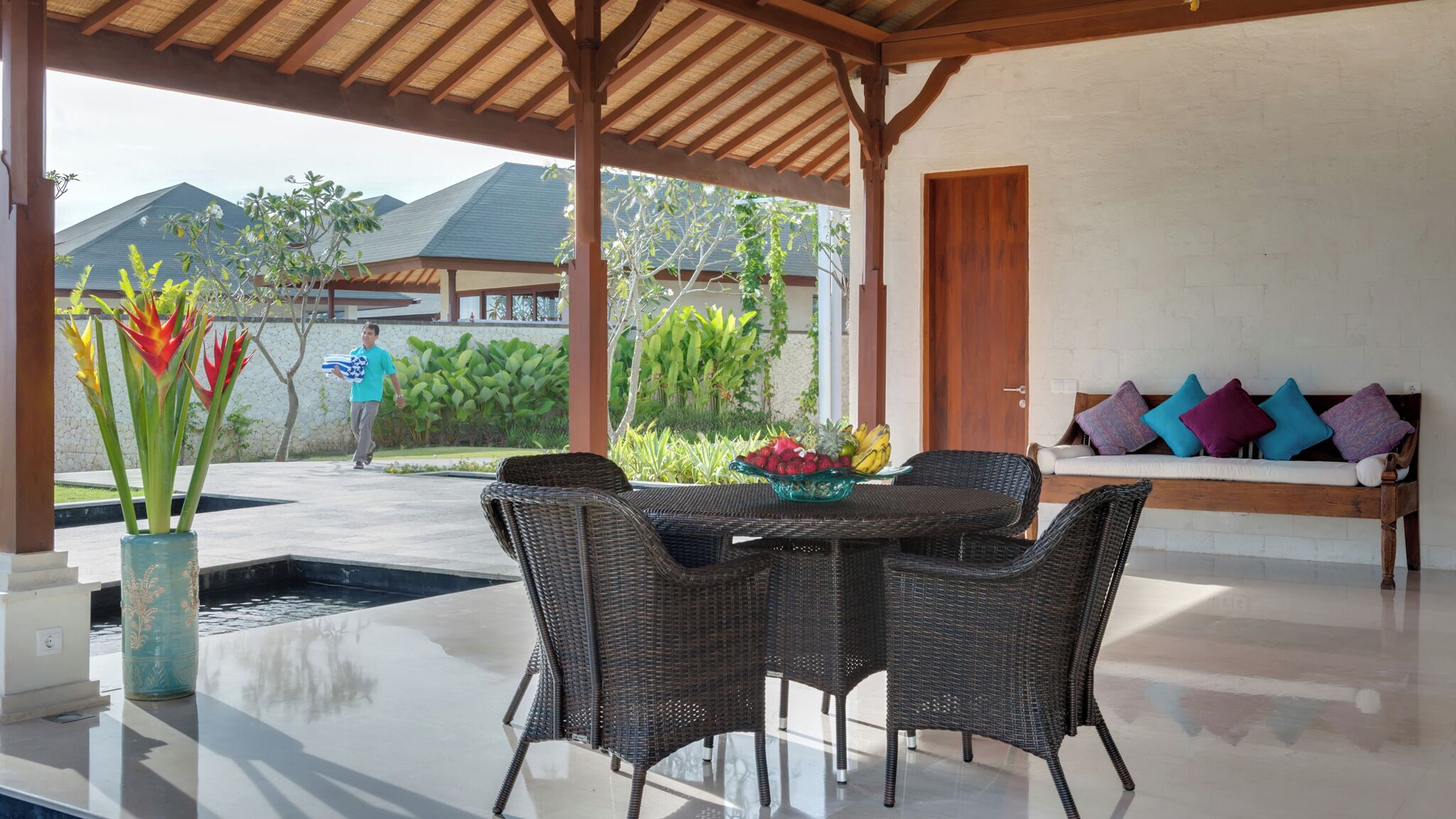 An outdoor patio with wicker furniture, a glass-top table, and a bowl of fruit.