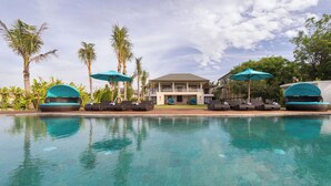 A poolside area with lounge chairs and umbrellas, a building with a balcony, and palm trees. - Villa Rose by Elite Havens (The Bukit)
