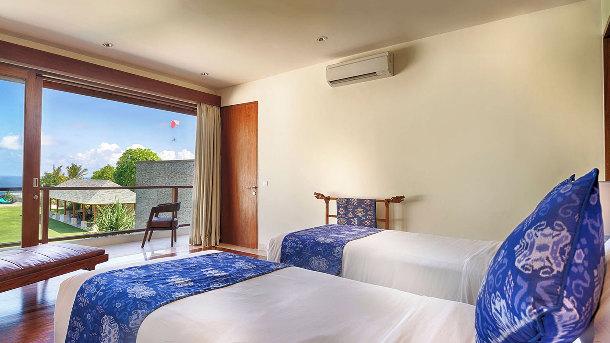 A hotel room with two beds, a balcony with a view of the sea, and an air conditioning unit on the wall.
