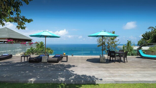 Eine Holzterrasse mit Sitzgelegenheiten im Freien, zwei Sonnenschirmen und Blick auf das Meer.