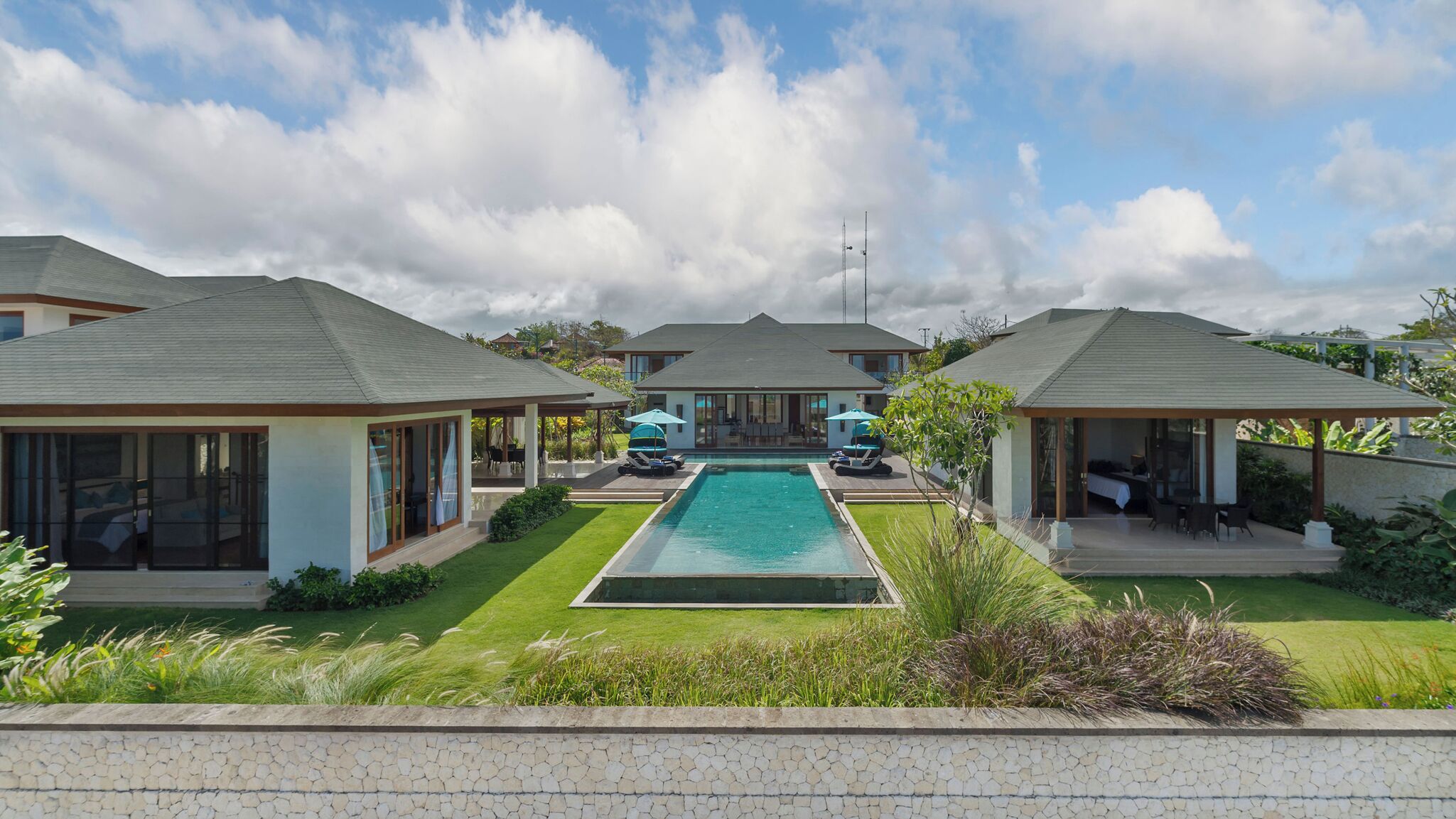 Un resort moderno con piscina central, varias villas para huéspedes y exuberante jardinería.