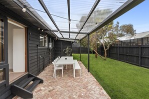 Une terrasse couverte avec une table et des chaises, un sol en briques et une clôture en bois en arrière-plan.