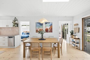 Une cuisine moderne avec des meubles blancs, une table à manger en bois et quatre chaises, ainsi qu’une grande fenêtre qui laisse entrer la lumière naturelle.