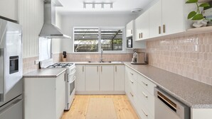 Eine moderne Küche mit weißen Schränken, einem Edelstahlherd, einem Backofen, einer Spüle und einem Fenster mit Blick ins Freie.