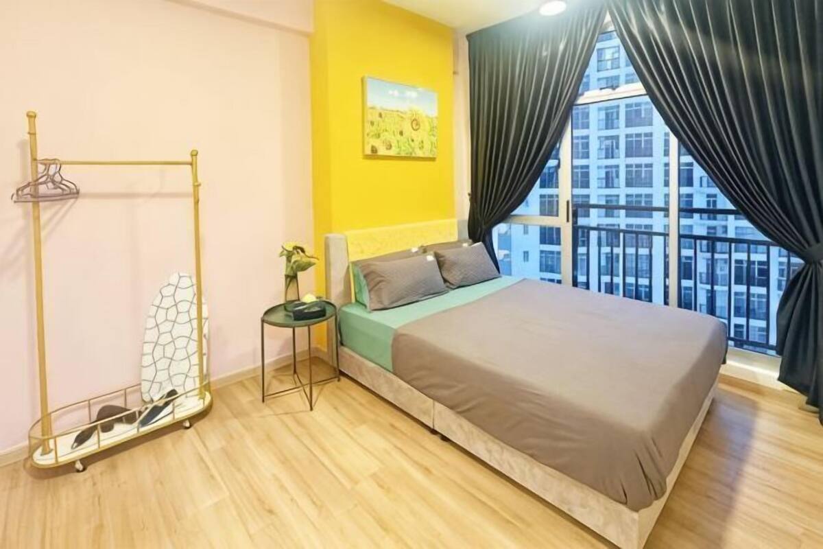 A bedroom with a bed, a small table, a hanging rack, and a window with curtains.
