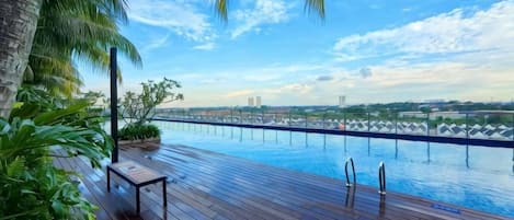 Une piscine à débordement dotée d’une terrasse en bois, entourée de plantes tropicales et de palmiers.