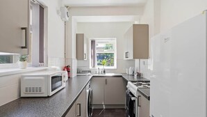A modern kitchen with white cabinets, a built-in oven, a microwave, and a stove. - 2 bed Home with Free Parking (Walsall)