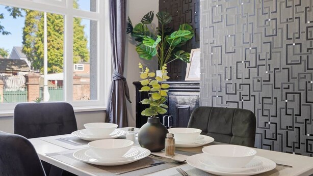 A dining area with a table set for four, a vase with yellow flowers, and a patterned wall. - 2 bed Home with Free Parking (Walsall)
